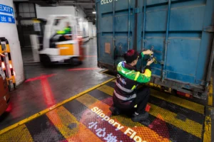 Worker securing blue shipping container at dock
